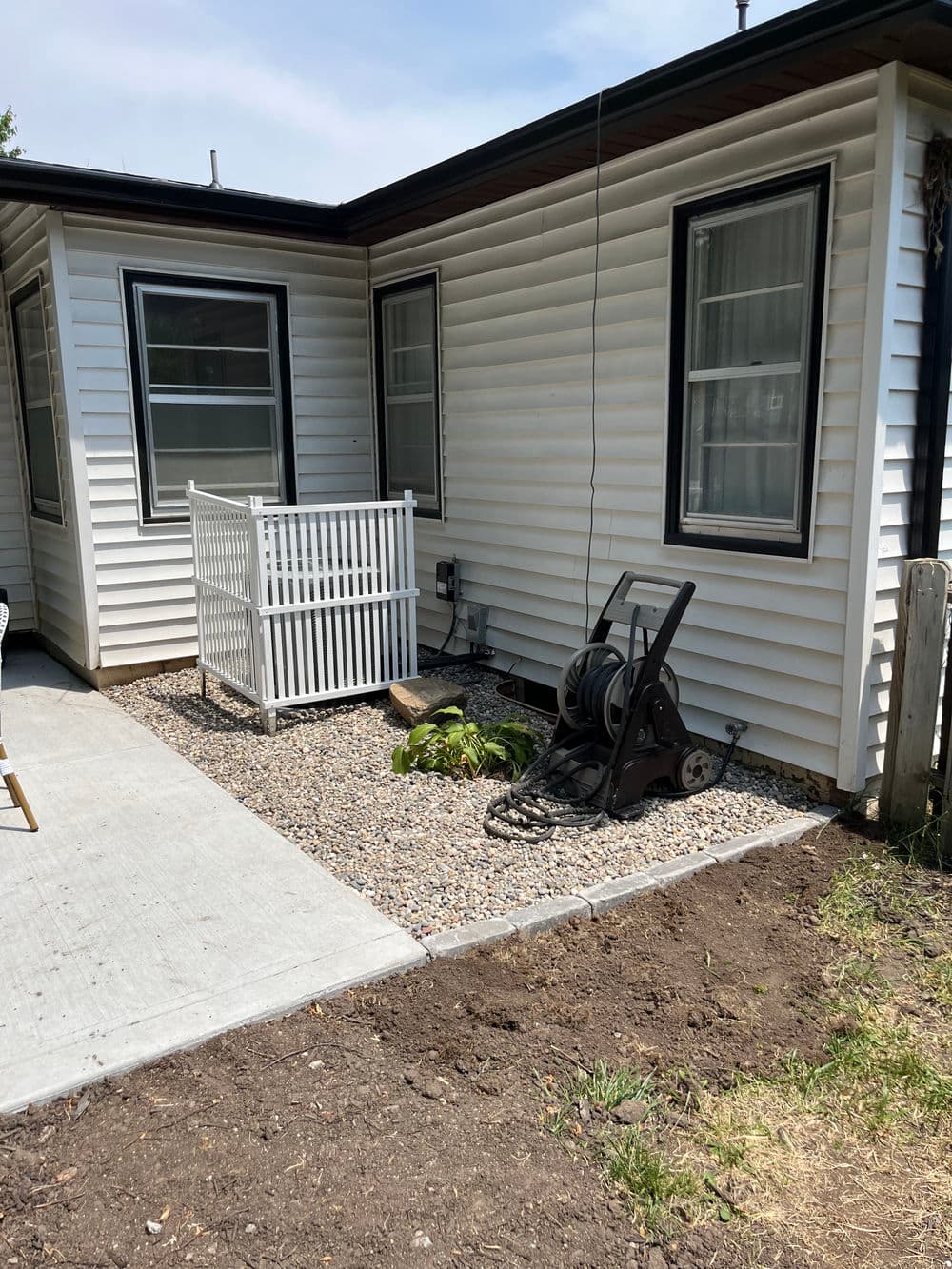 Modern home exterior with gravel landscaping, patio area, and garden hose reel.