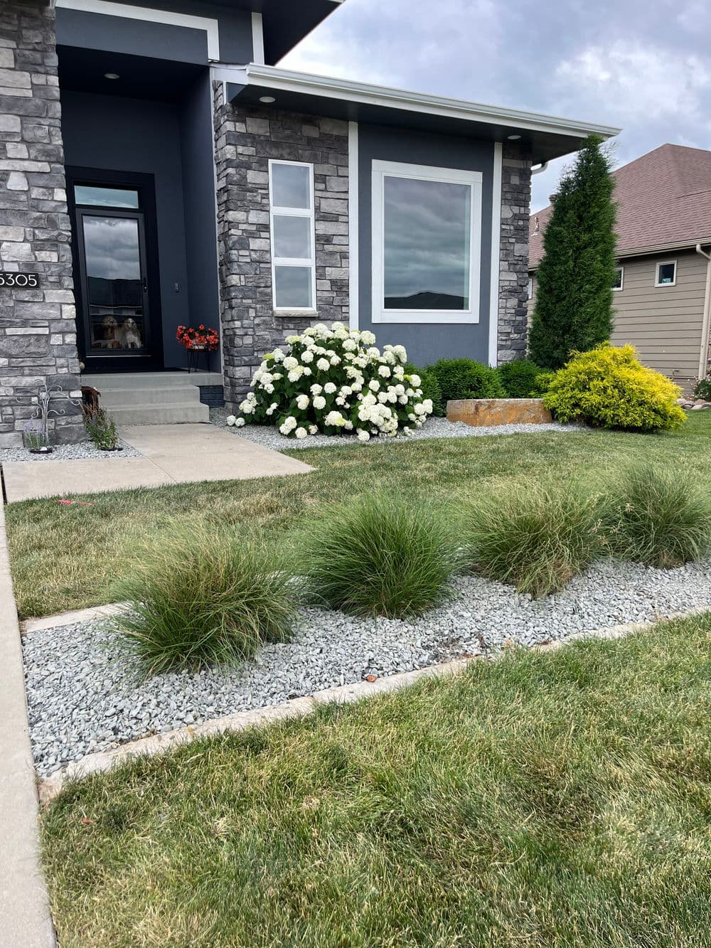 Modern home exterior with stone accents, flowering landscape, and well-maintained lawn.