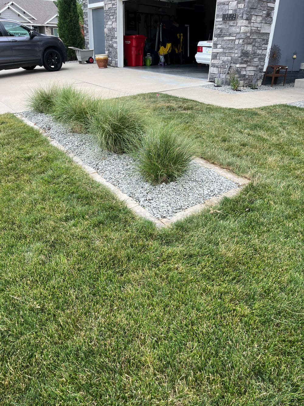 Landscaped yard with grass, decorative gravel, and ornamental grass clusters near a garage.
