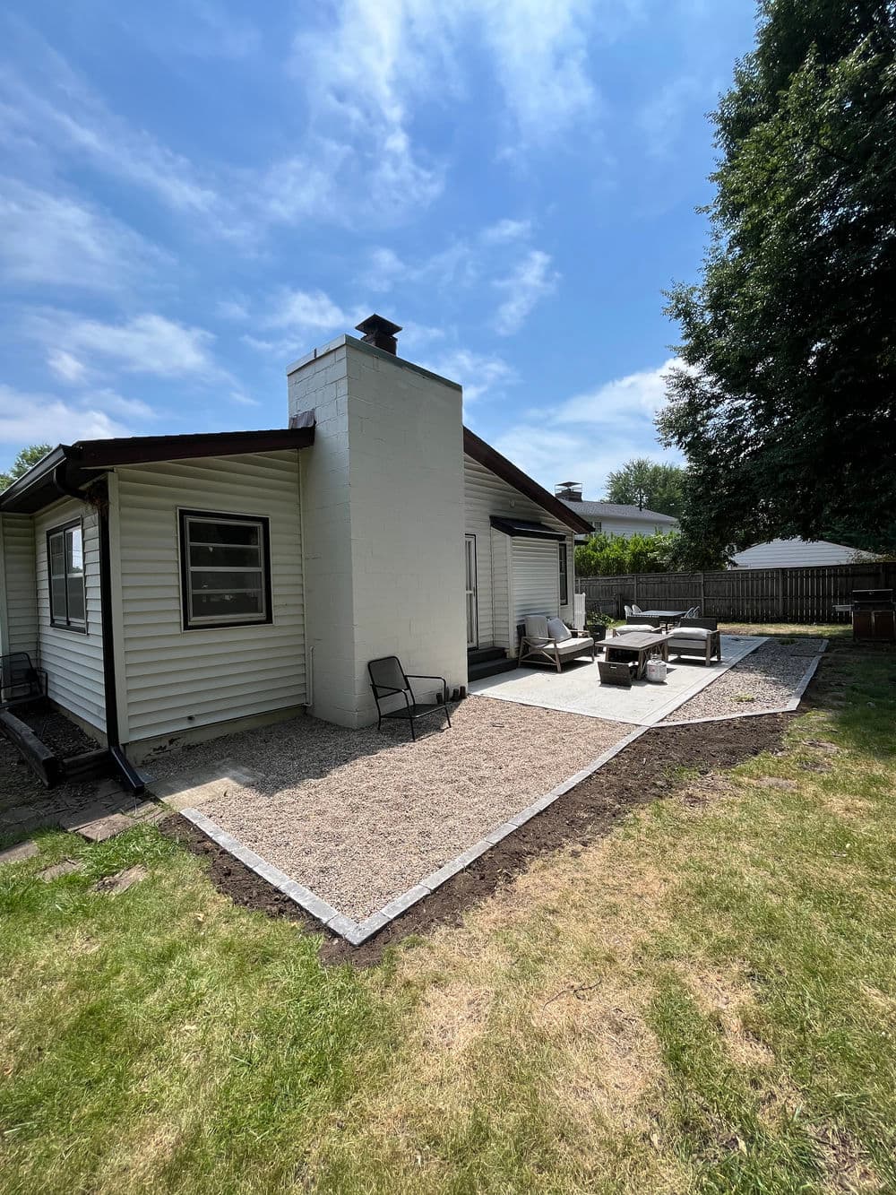 Modern backyard patio with seating area, gravel landscaping, and sunny blue sky.