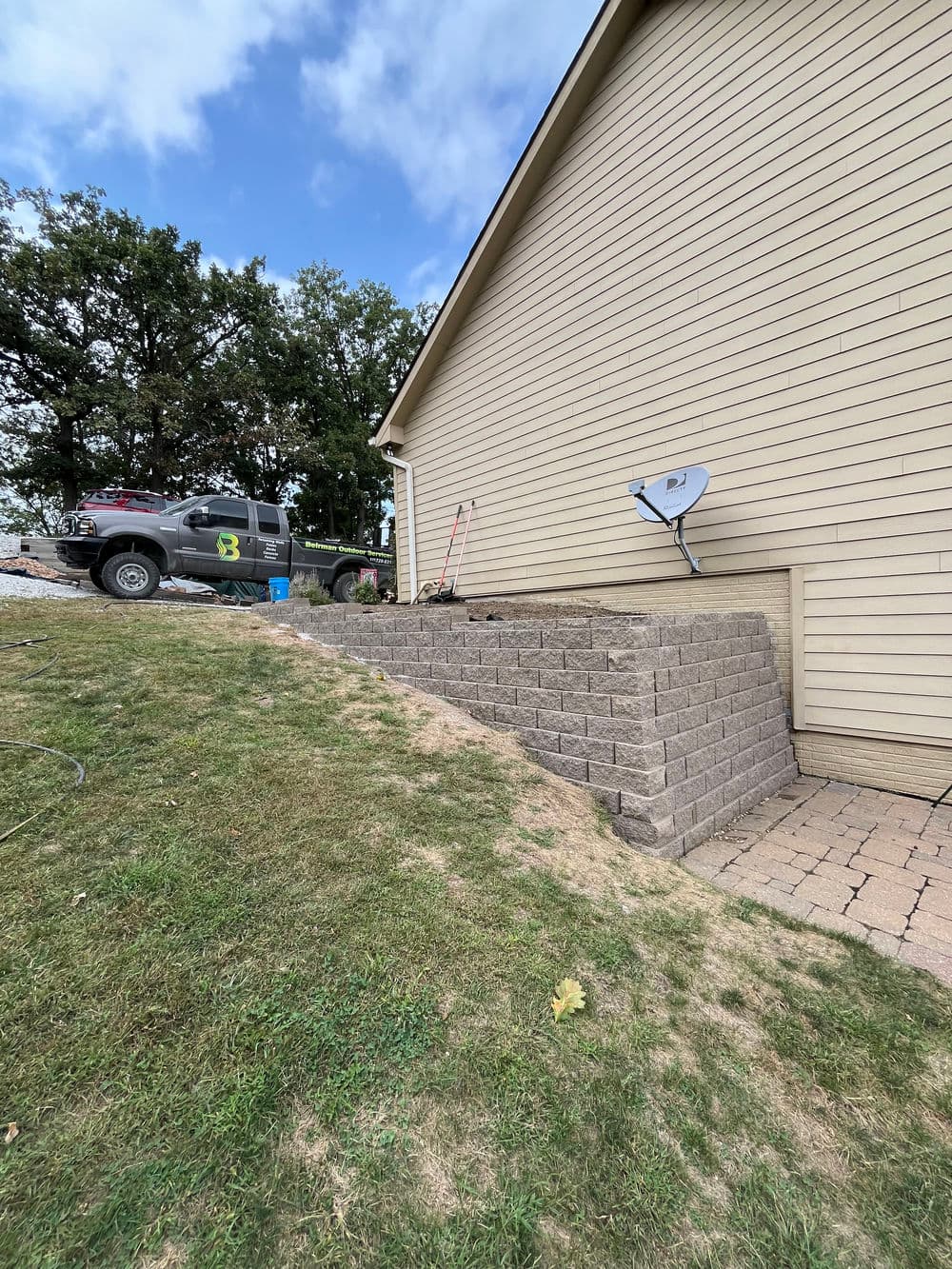 Retaining wall installation beside a house with a truck and satellite dish visible.