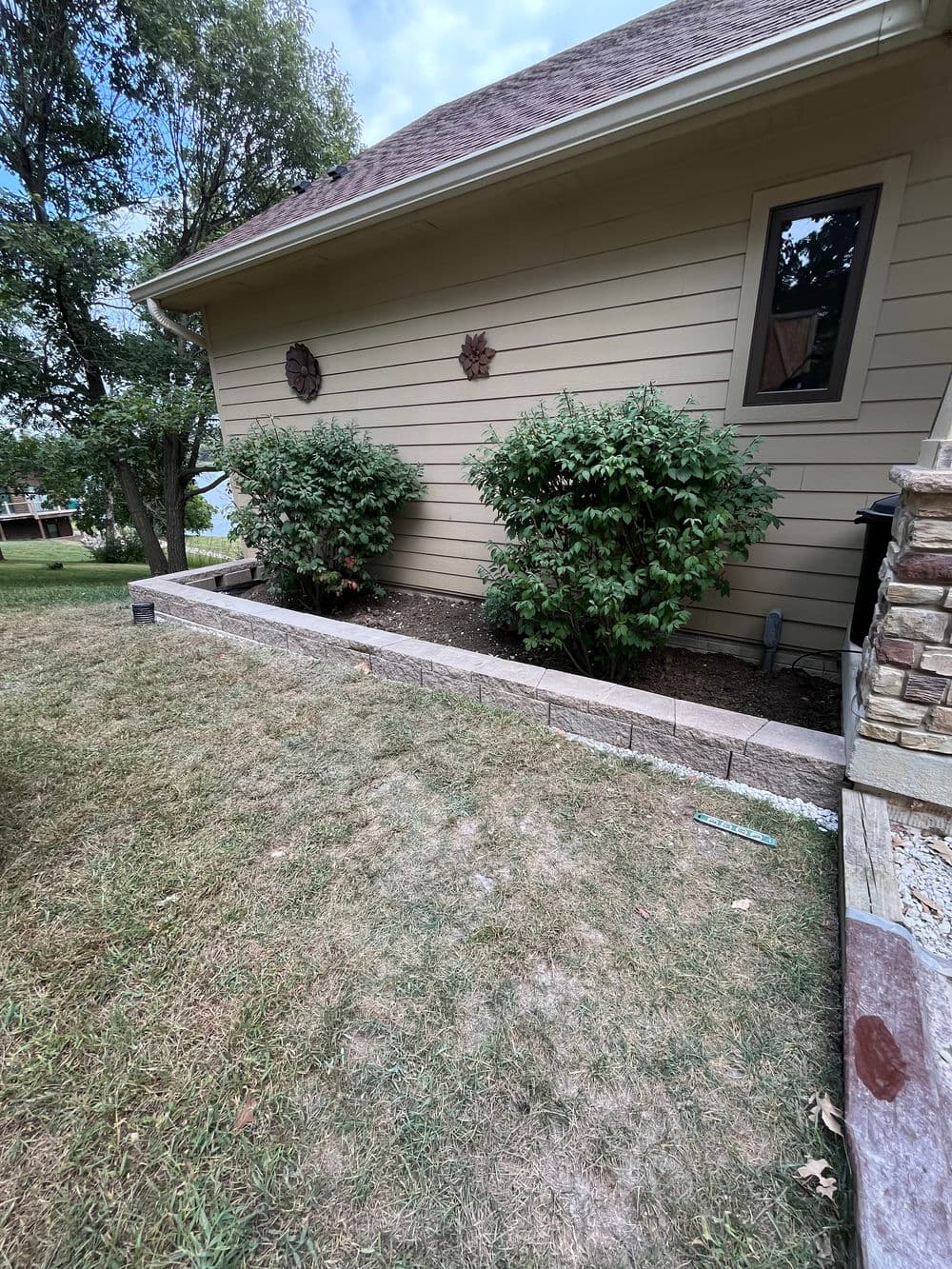 Landscaped side yard with shrubs, stone border, and a house in the background.