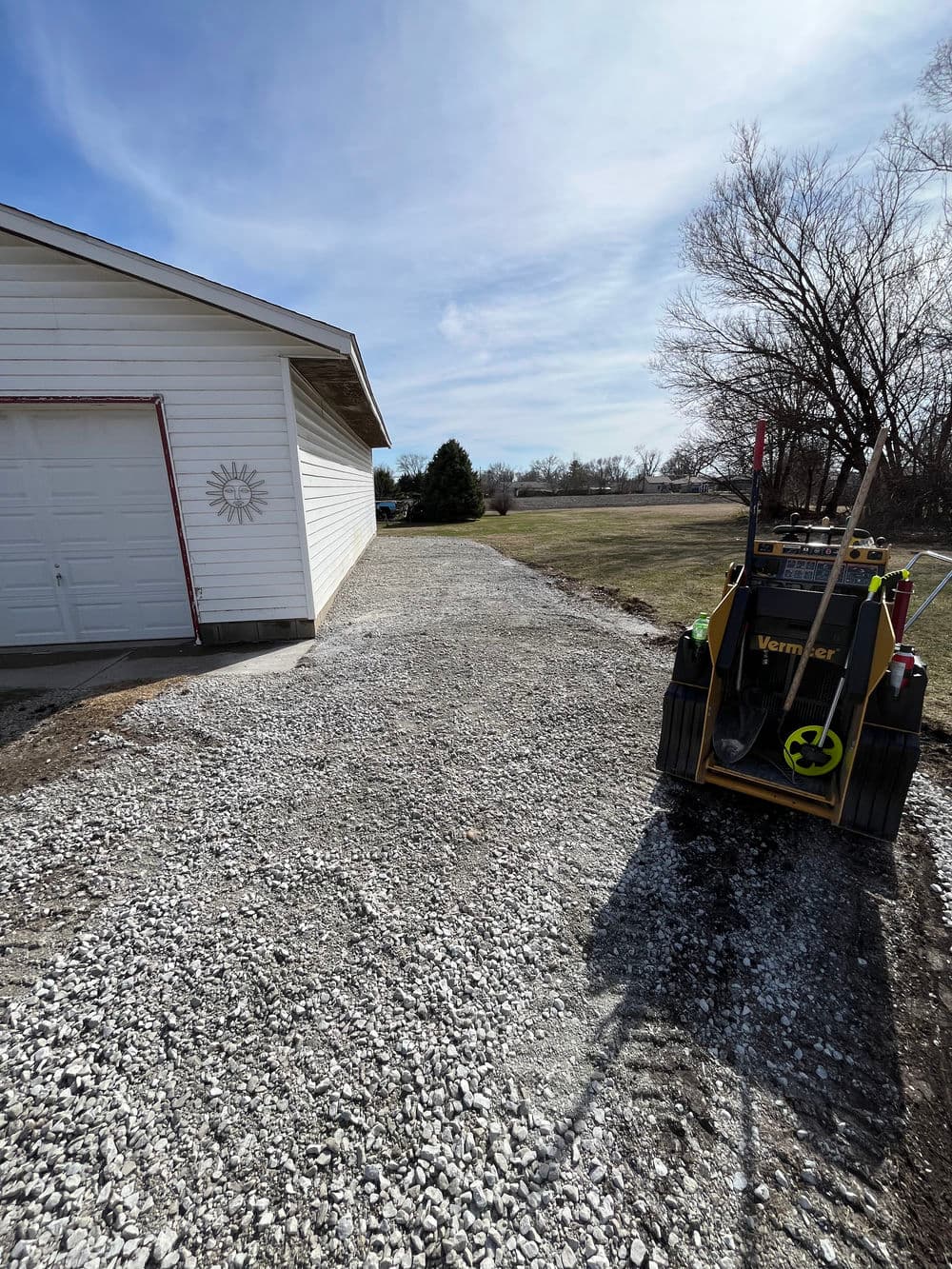 Gravel driveway leading to a house with a lawn and construction equipment nearby.