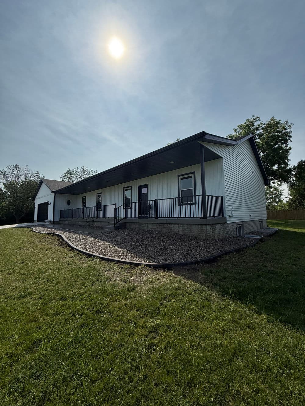 Modern white house with a front porch, surrounded by greenery under a sunny sky.