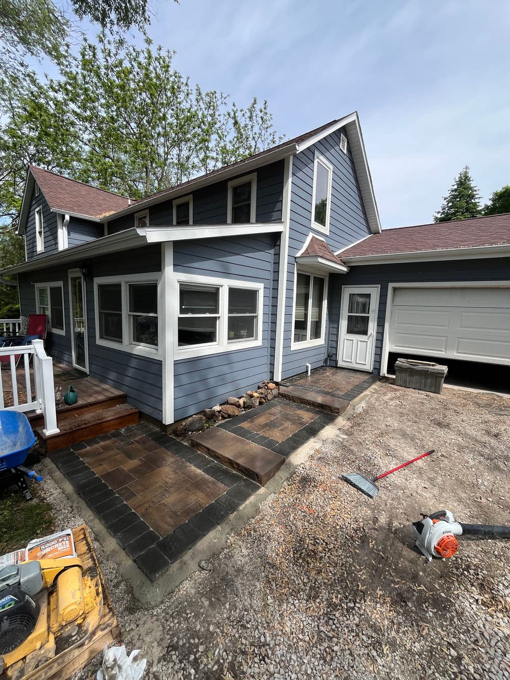 Modern blue house exterior with newly paved pathway and garage, surrounded by trees.