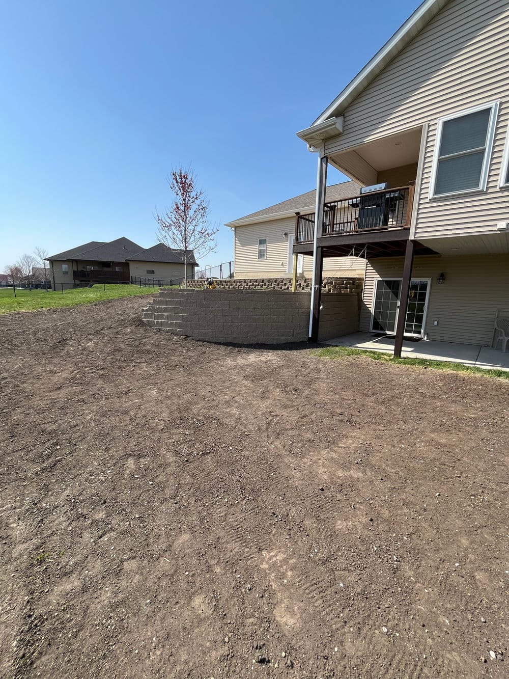 Backyard landscape featuring a patio with stairs, adjacent to a home and open green space.
