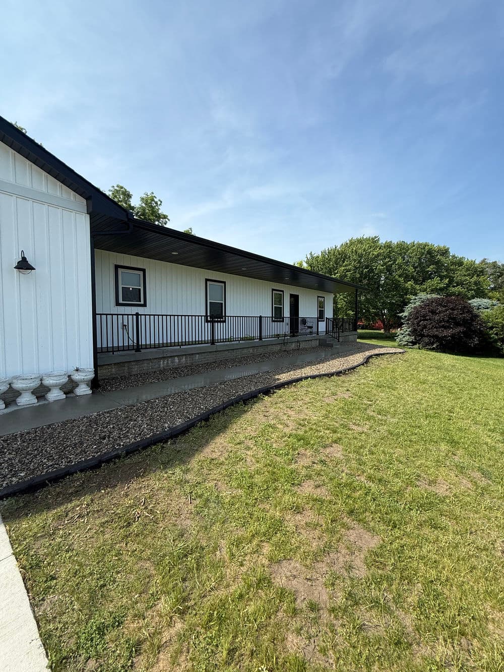 Modern white house with a porch, surrounded by green lawn and trees, under clear blue sky.