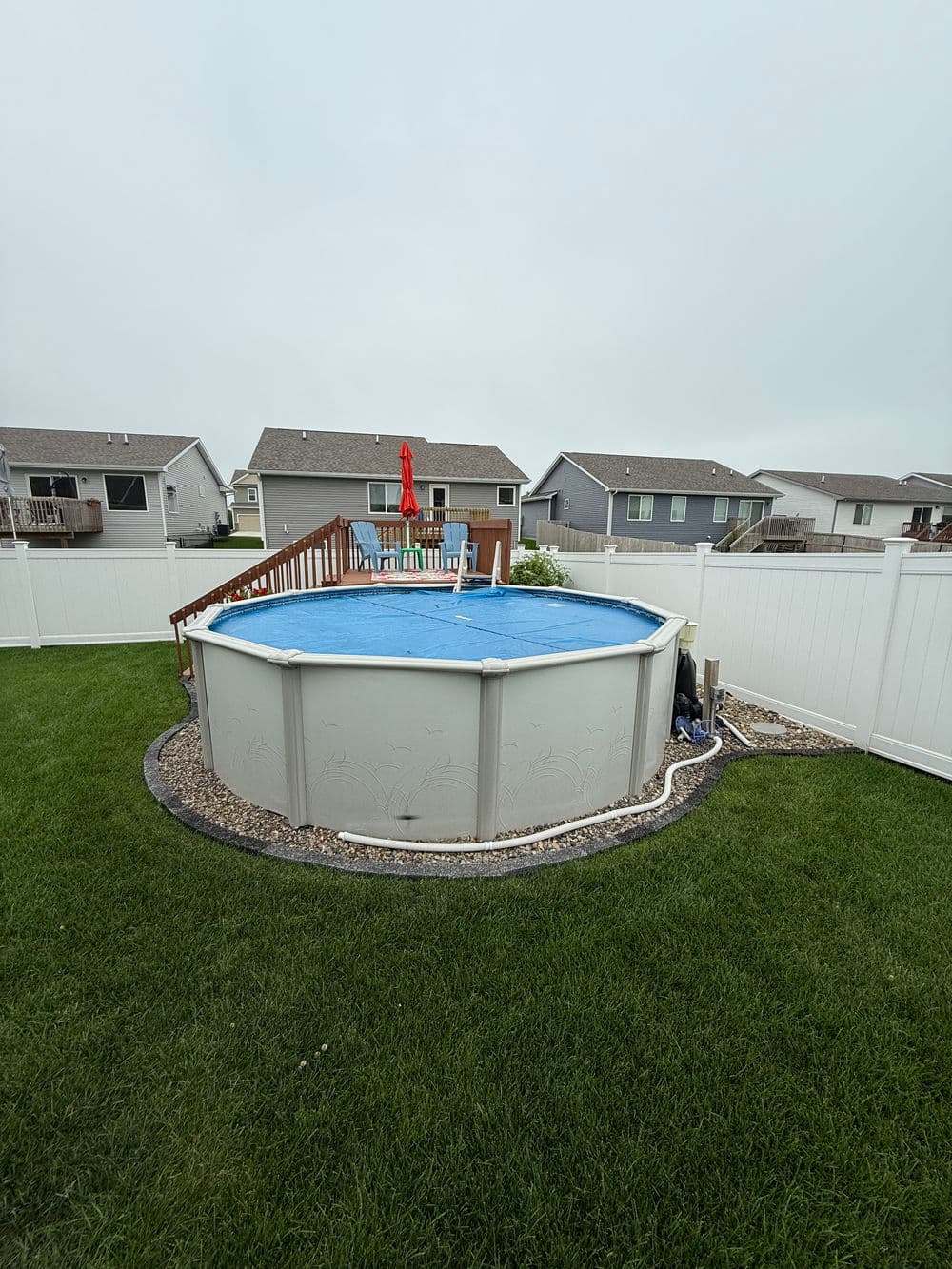 Above-ground pool surrounded by green grass and wooden deck in a residential backyard.