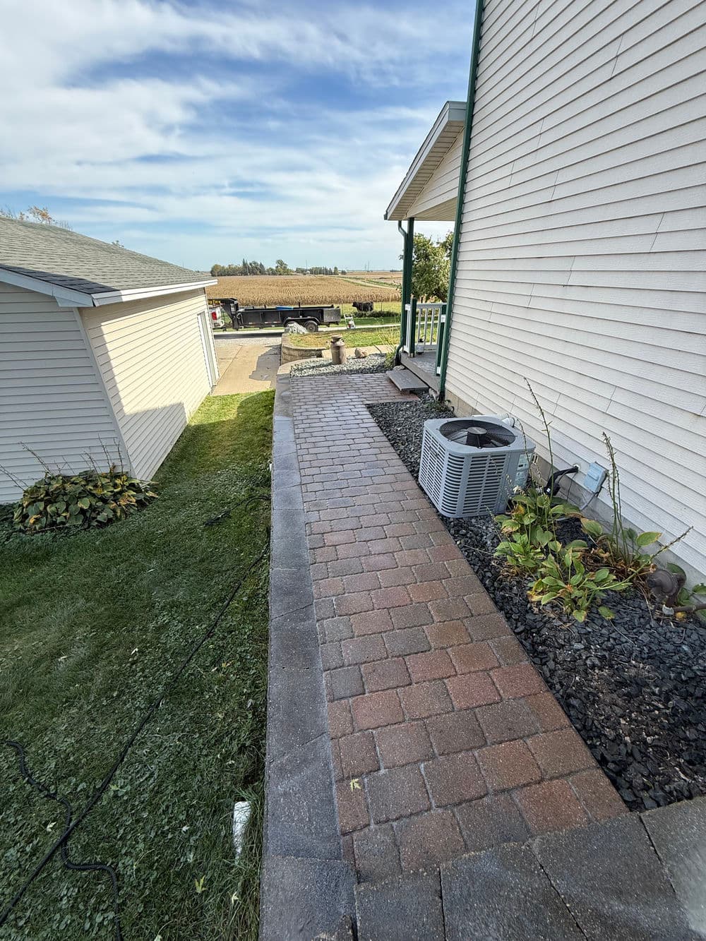 Paved walkway beside a house with landscaping, air conditioning unit, and clear sky.