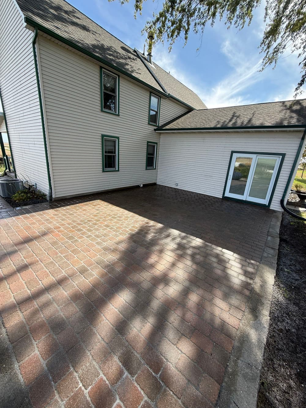 Newly paved patio area beside a two-story house with light-colored siding and large windows.