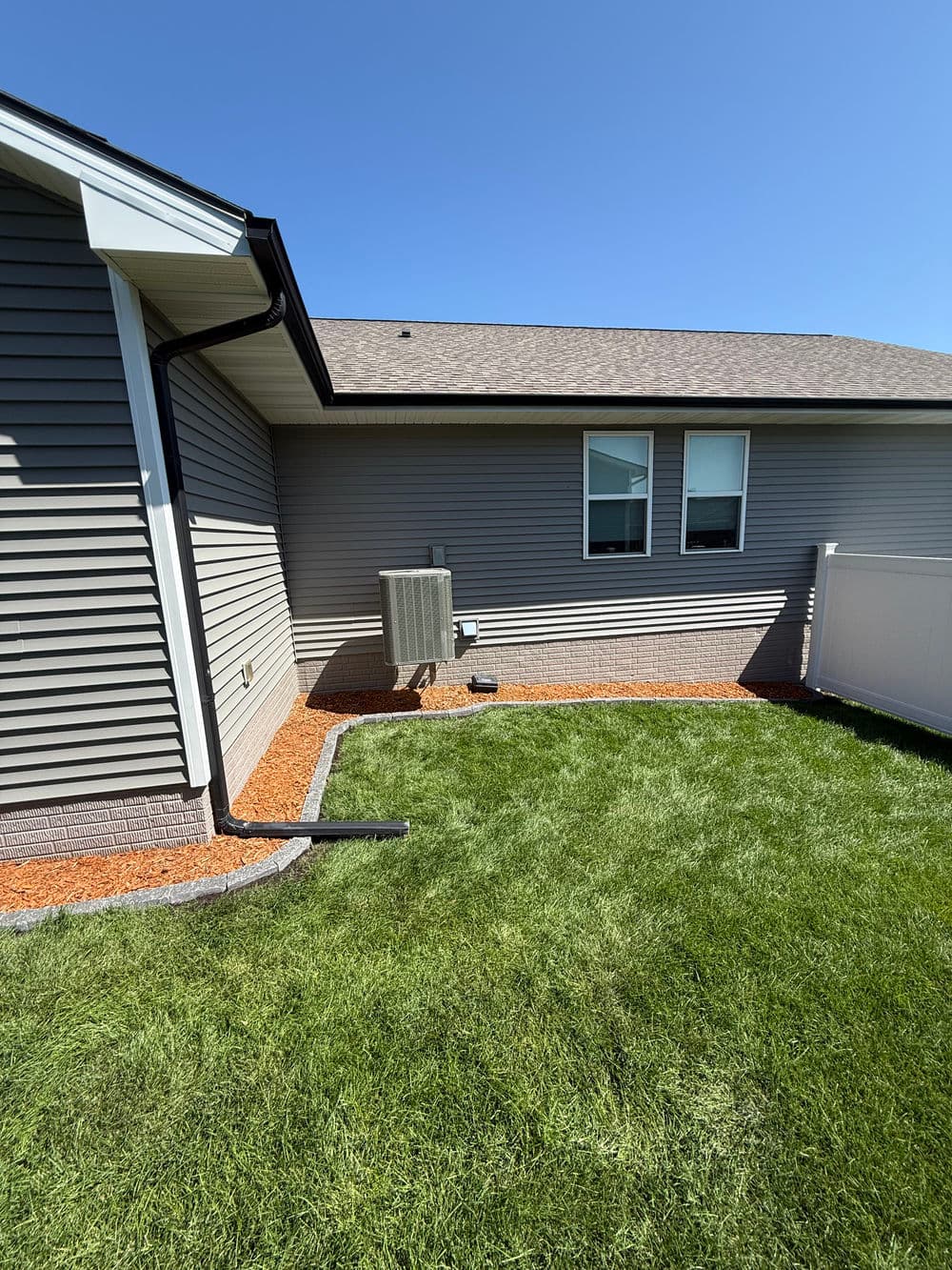 Newly landscaped backyard with grass, stone borders, and an air conditioning unit.