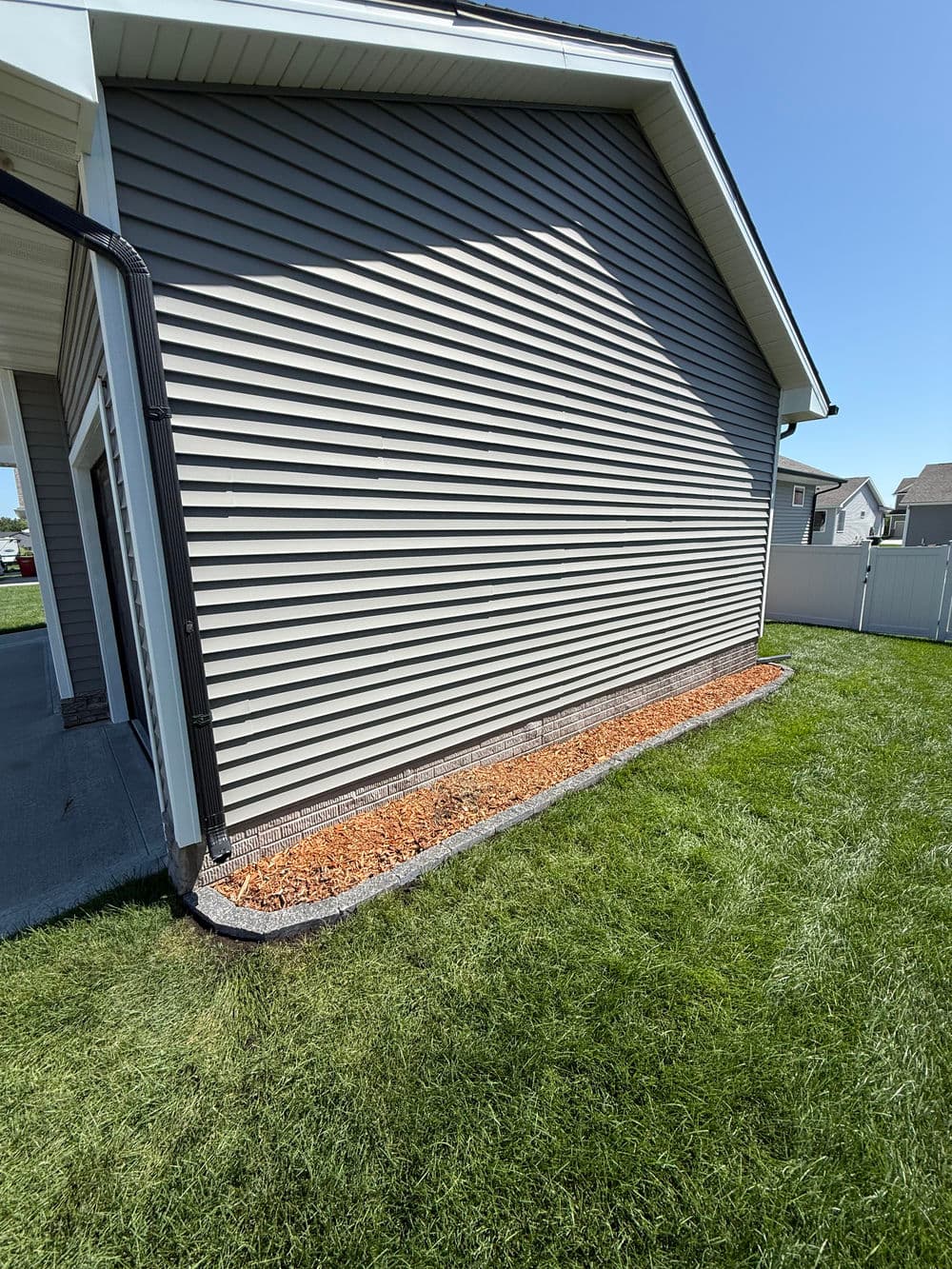 Side view of a house with gray siding, landscaped border, and green lawn.