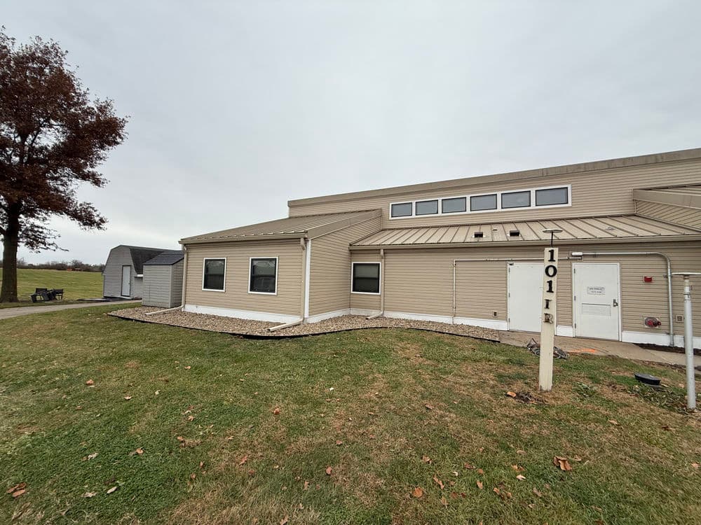 Exterior view of a beige commercial building with a sloped roof and grassy area.