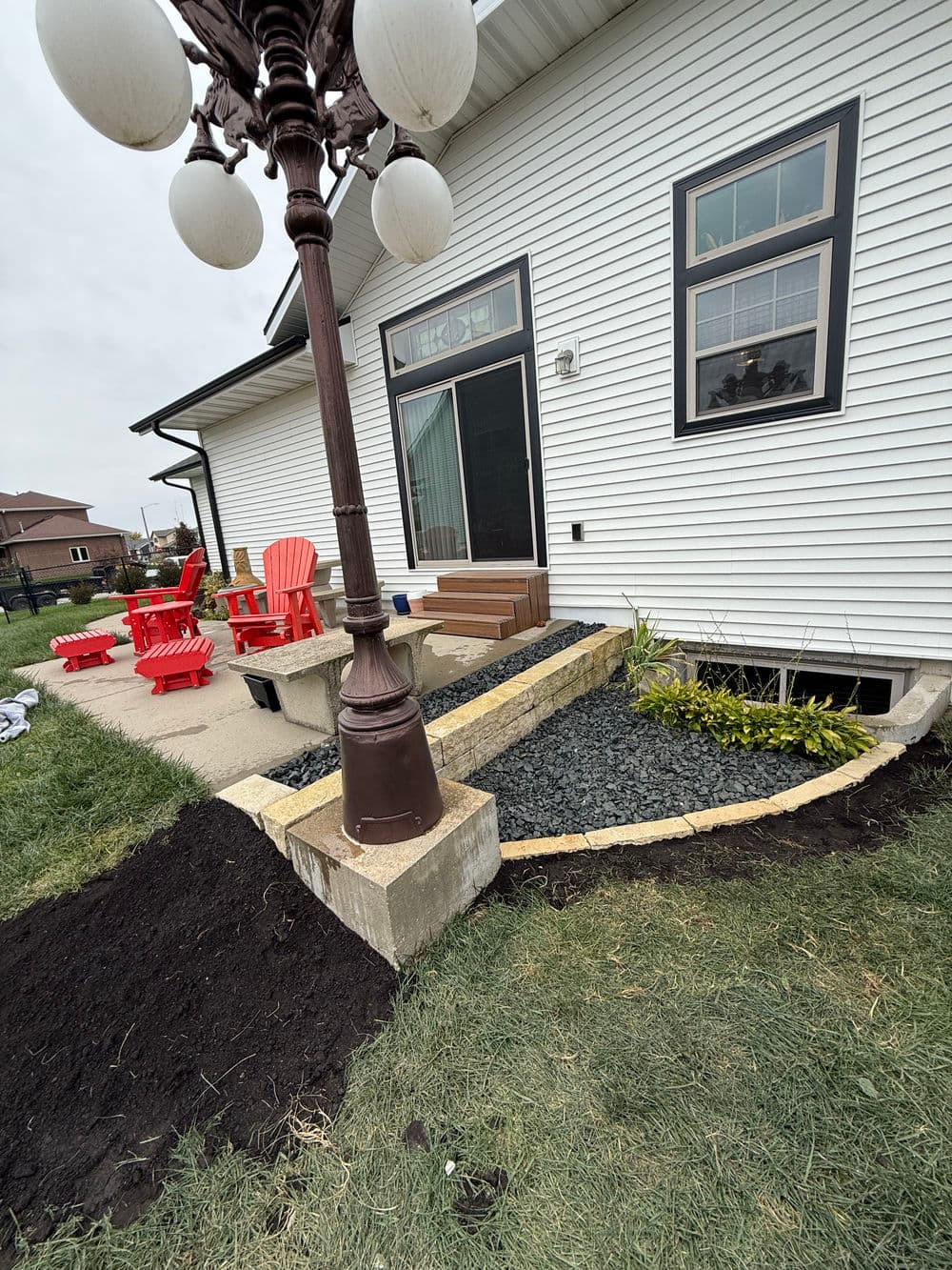 Backyard patio area featuring a lamp post, red chairs, and stone landscaping.
