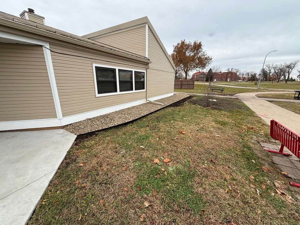 Newly landscaped yard beside a beige house with a gravel border and park pathway.